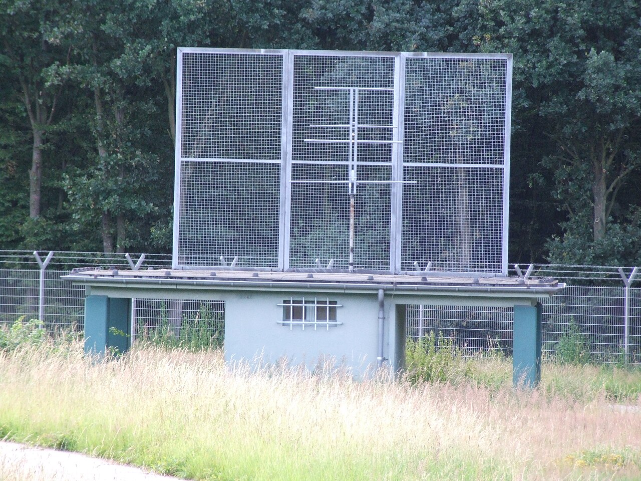 中指点标台站实景：设备小屋上架一面金属网屏天线，立在草地围栏内