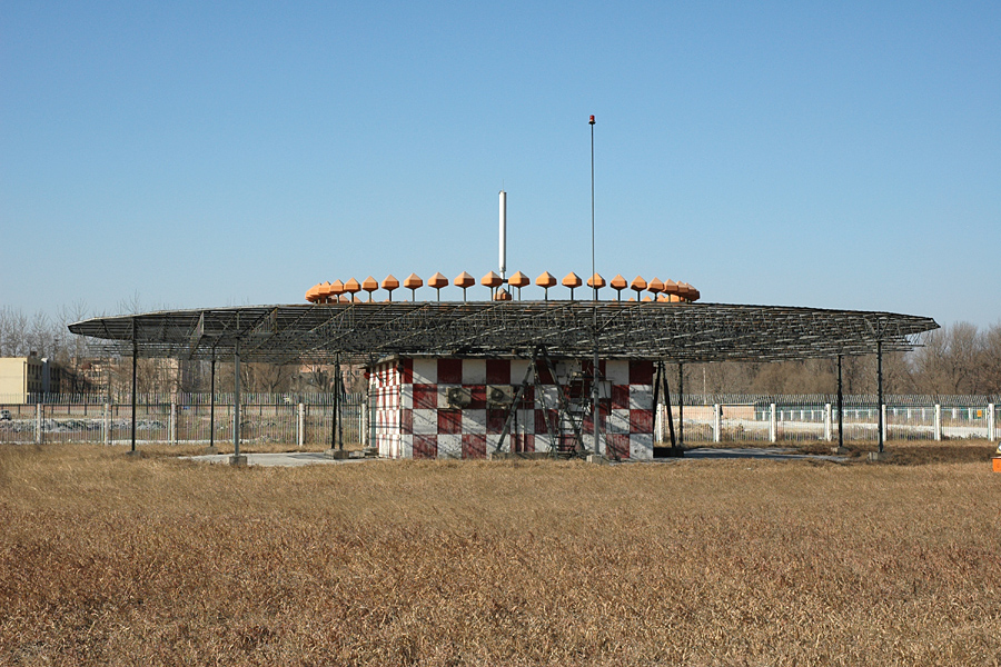 北京首都机场 D-VOR 实景：盘沿橙色边带天线阵清晰可见，盘下是红白格外墙的机房