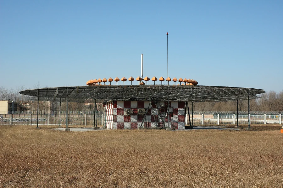 北京首都机场 D-VOR 实景：盘沿橙色边带天线阵清晰可见，盘下是红白格外墙的机房